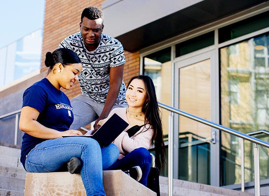Three UCR students review notes on a laptop together. 