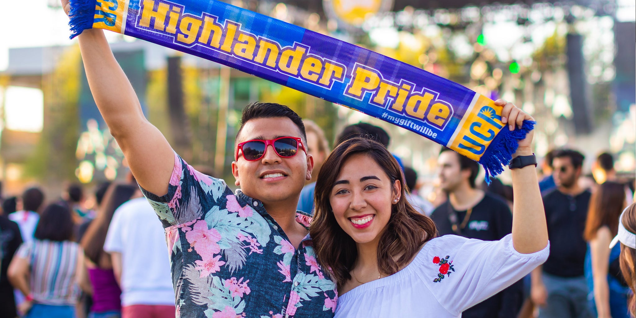 Two students post with a Highlander Pride scarf at a campus event.