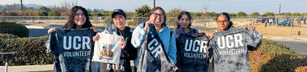 Students holding up UCR Volunteer shirts at an event.